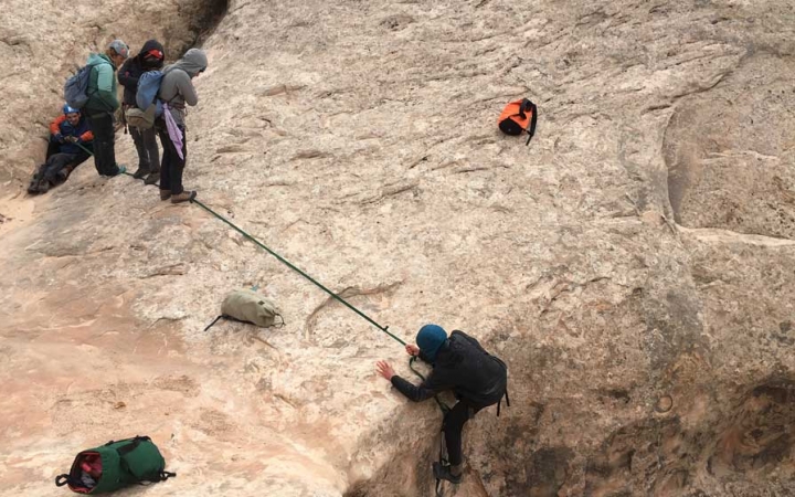 A person wearing safety gear is secured by a rope as they rappel into a canyon. 